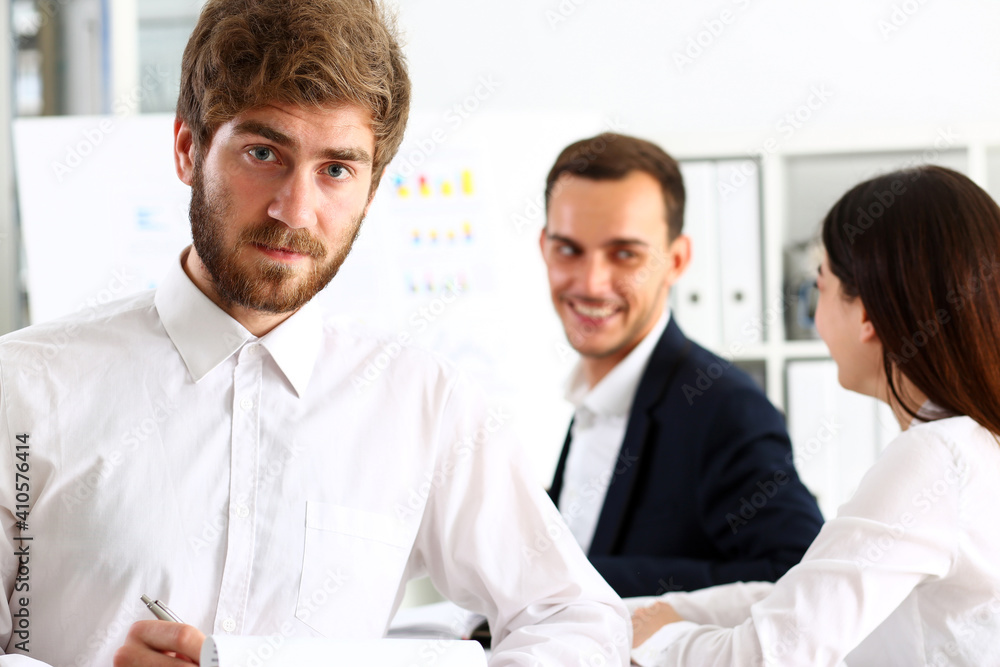 Handsome smiling bearded man in office look in camera with colleagues in background. White collar worker, modern lifestyle, graduate college study, report idea, coach train visit, make note concept