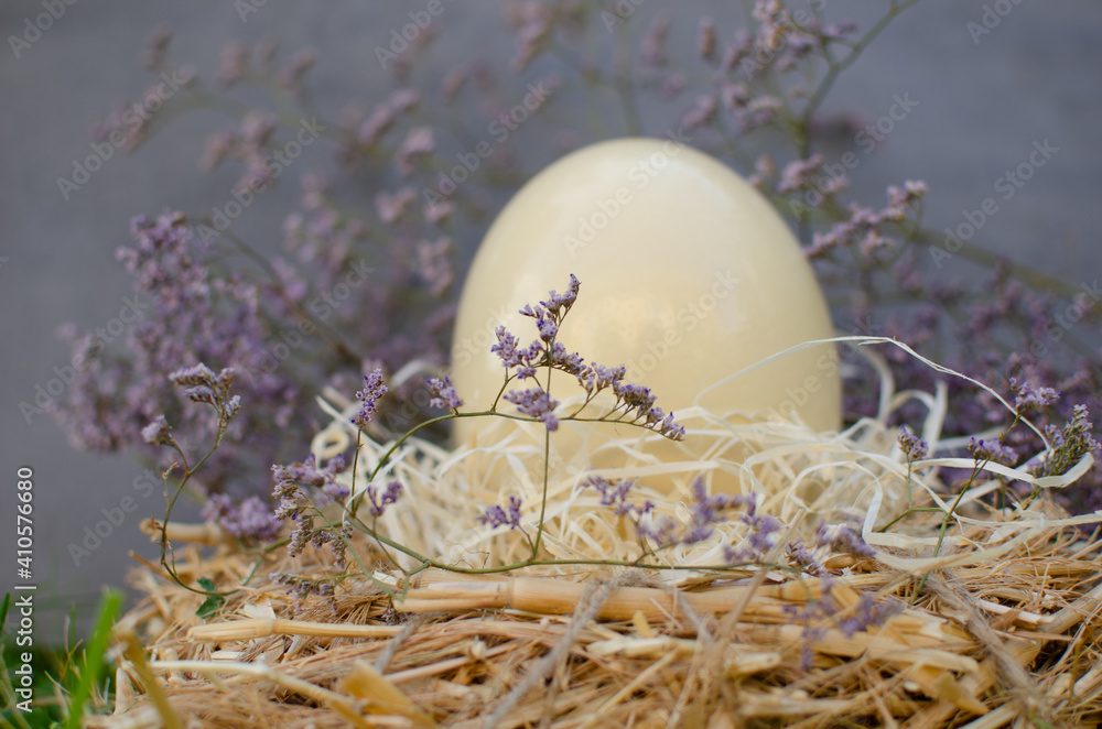 Obraz premium In a nest of hay lies a large fresh ostrich egg, decorated with purple flowers. Easter theme, holiday. Happy easter card with copy space for text in minimal easter style