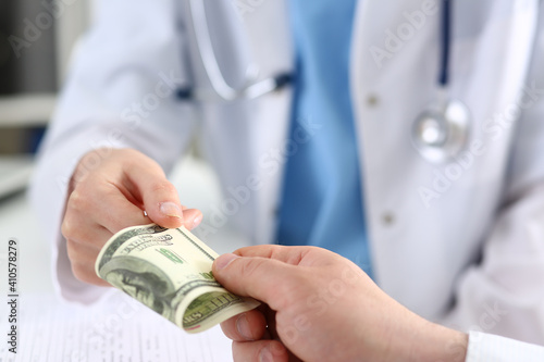 Female doctor hold in hands bunch of hundred dollars banknotes take or give them. Prestige and high paid job, encash treatment, illegal drug fraud, anonymous visitor, private visit, reform concept photo
