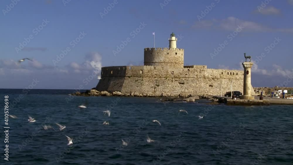 Rhodes Greece the lighthouse of Agios Nikolaos at the entrance of the port of the city we see many seagulls flying over the sea following a flock of small fish Rhodes Greece the lighthouse of Agios Nikolaos at the entrance of the port of the city we see many seagulls flying over the sea following a flock of small fish