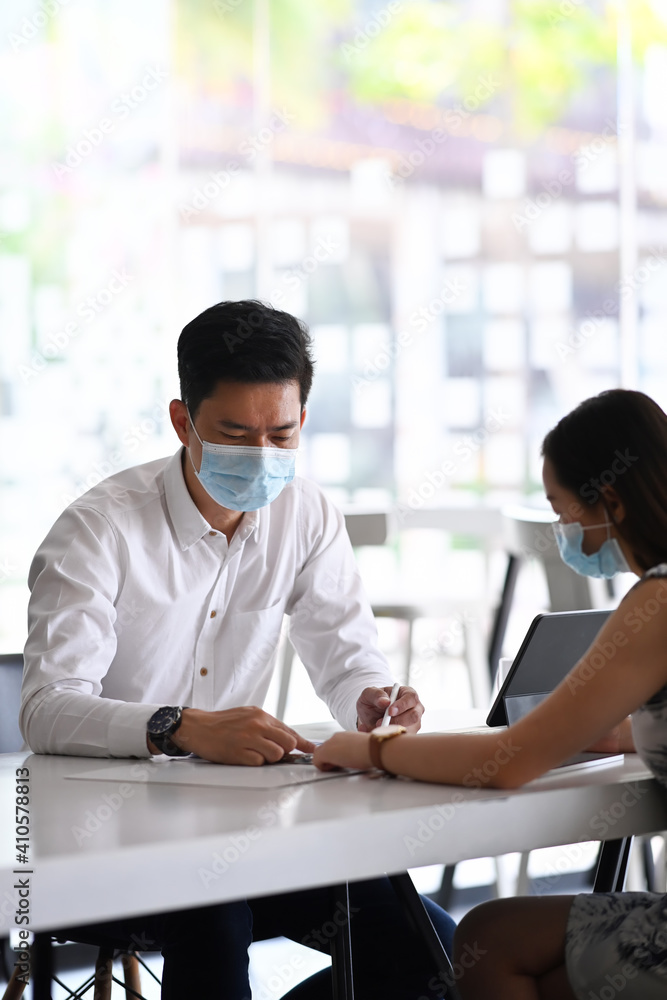 Obraz premium Two business people wearing protective mask discussing marketing strategy at office table.