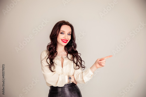 Beautiful young girl student, business woman smiles, pointing and looking away over gray background