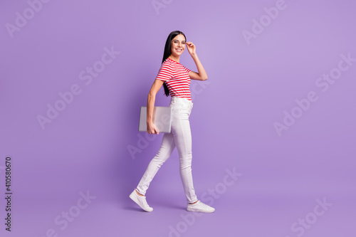 Full length profile side of charming young woman adjust glasses hold laptop walk copyspace isolated on violet color background