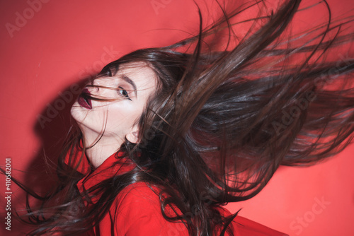 Crazy girl waving her hair. Woman with stylish makeup and long hair posing in total red outfit. Fashion concept. Girl on mysterious face in red formal jacket, red background.