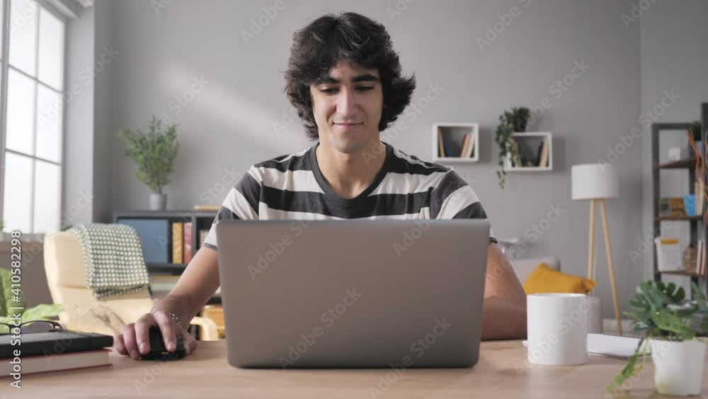 young man sits at his desk opens laptop and start working zoom out motion,arab middle eastern male student opening and using computer from home in modern living room young man sits at his desk opens laptop and start working zoom out motion,arab middle eastern male student opening and using computer from home in modern living room