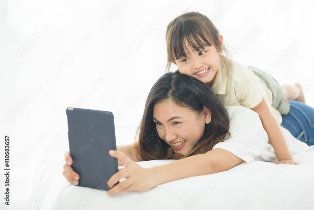 Happiness Asian young mother and little cute daughter lying on bed in the house using labtop for entertain, family joyful together in the house on holiday Happiness Asian young mother and little cute daughter lying on bed in the house using labtop for entertain, family joyful together in the house on holiday