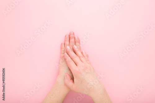 Mature woman hands on light pink table background. Pastel color. Closeup. Point of view shot. Care about clean, beautiful, soft hands skin and nails in old ages. Top down view.
