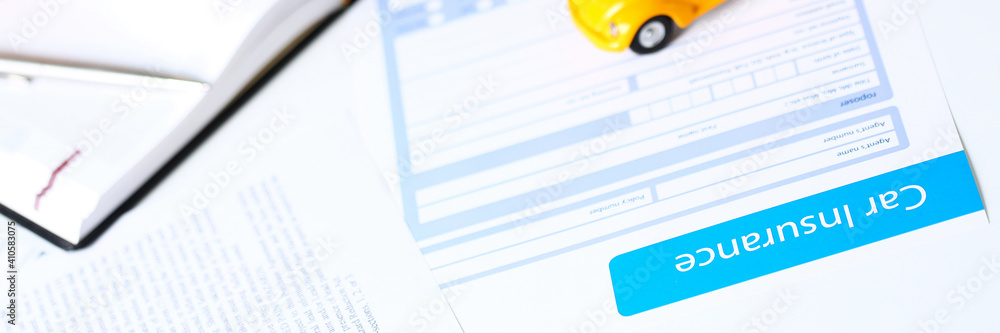 Insurance form lying on table with unrecognizable yellow toy car closeup. Driver money loss prevention, secure road trip, harmless drive idea, owner protective offer concept