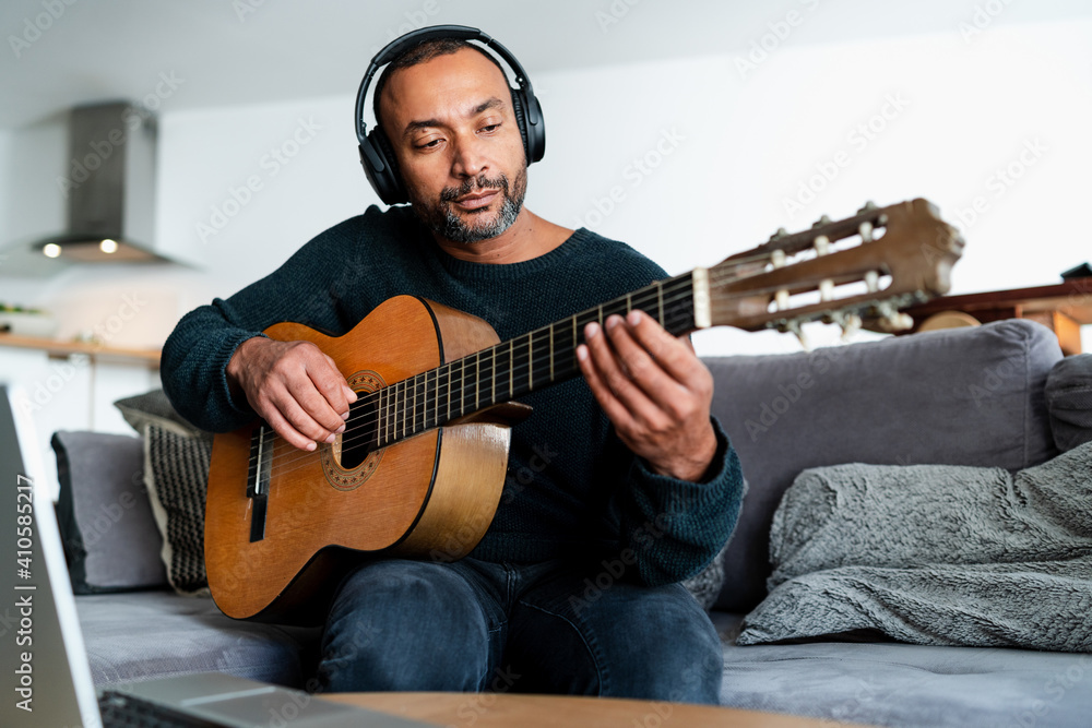 Obraz premium Black man playing the guitar at home and using a laptop