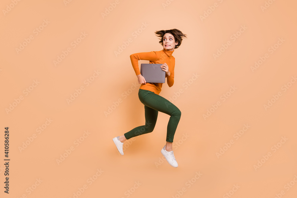 Full size profile side photo of young scared afraid nervous stressed girl run in air hold laptop isolated on beige color background
