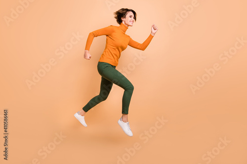 Full size profile side photo of young beautiful happy positive smiling girl running isolated on beige color background