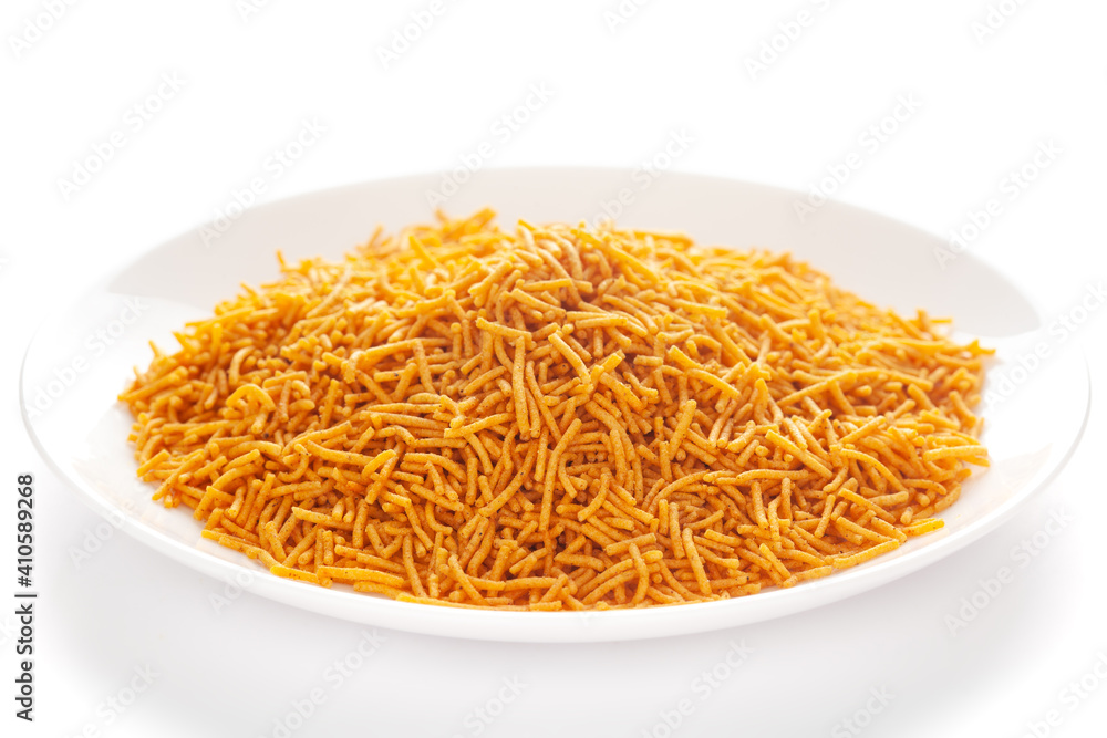 Spicy Aloo Bhujia in a white ceramic plate, made with Red chili, Potatoes, and Chickpeas. Pile of Indian spicy snacks (Namkeen), under backlight, side view