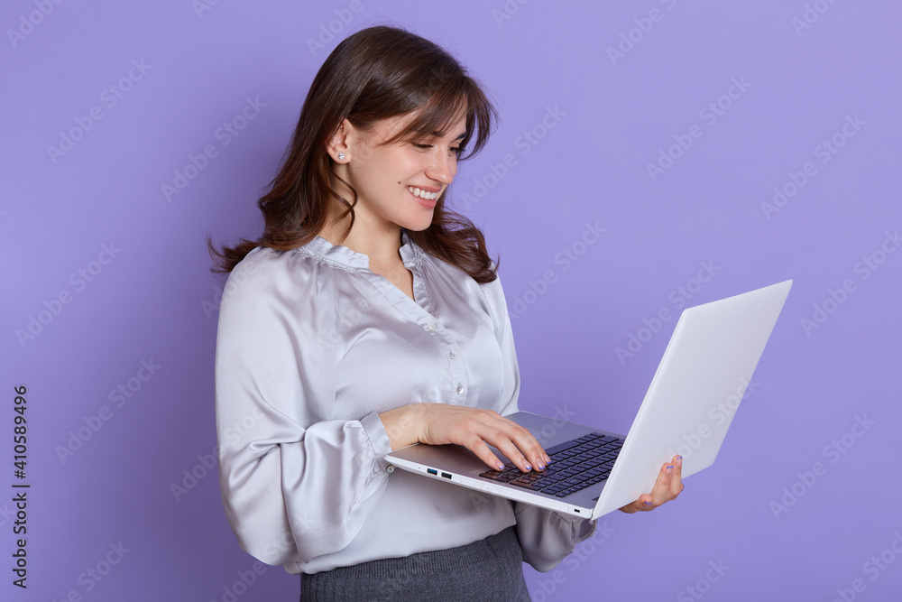 Portrait of cheerful young businesswoman working on laptop and smiling, female with portable computer in hands, being happy, wearing blouse and skirt, attractive lady browsing Internet for working. Portrait of cheerful young businesswoman working on laptop and smiling, female with portable computer in hands, being happy, wearing blouse and skirt, attractive lady browsing Internet for working.