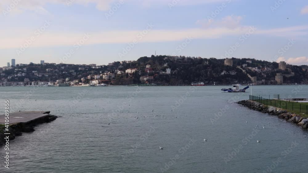 Seagulls Swimming At Bosphorus Strait With A Sailing Boat - Rumelihisari, Rumelian Castle With Uskudar On The Banks Of Bosporus In Istanbul, Turkey. - wide, static shot Seagulls Swimming At Bosphorus Strait With A Sailing Boat - Rumelihisari, Rumelian Castle With Uskudar On The Banks Of Bosporus In Istanbul, Turkey. - wide, static shot