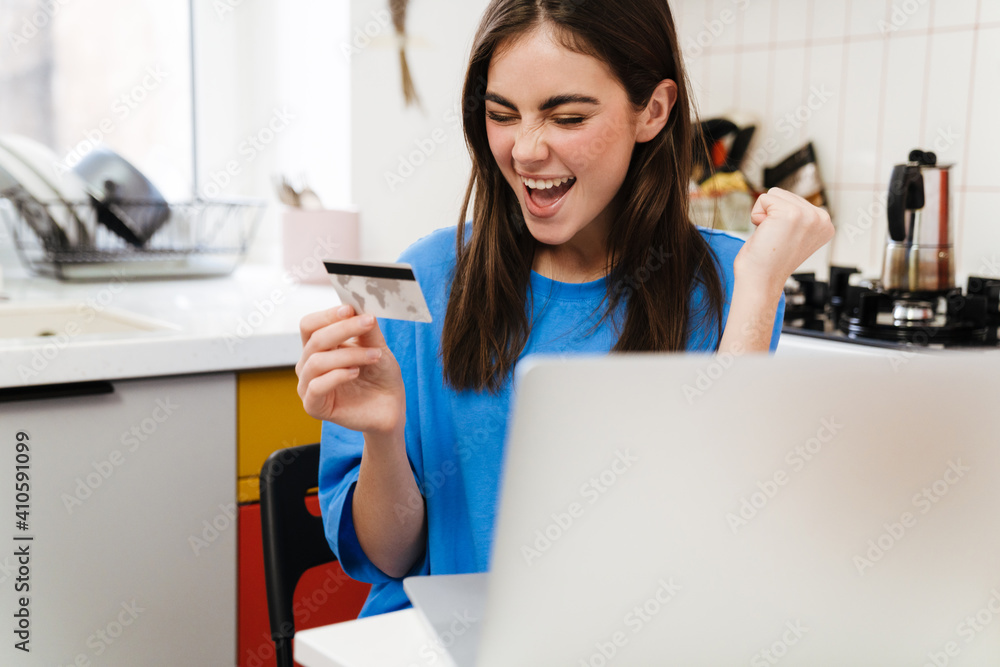 Excited girl making winner gesture and holding card and using laptop Excited girl making winner gesture and holding card and using laptop
