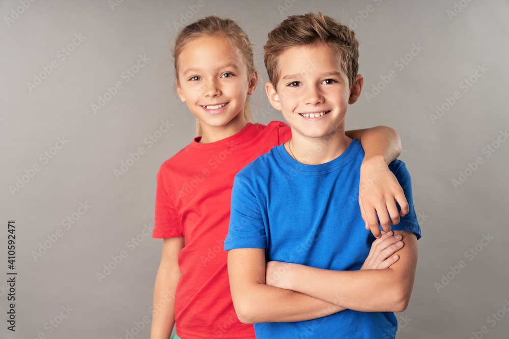 Cheerful boy and girl standing against gray background