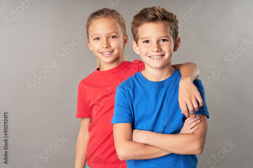 Cheerful boy and girl standing against gray background photo