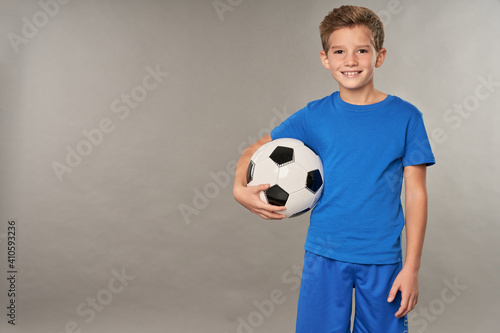 Cheerful boy with soccer ball standing against gray background © Friends Stock