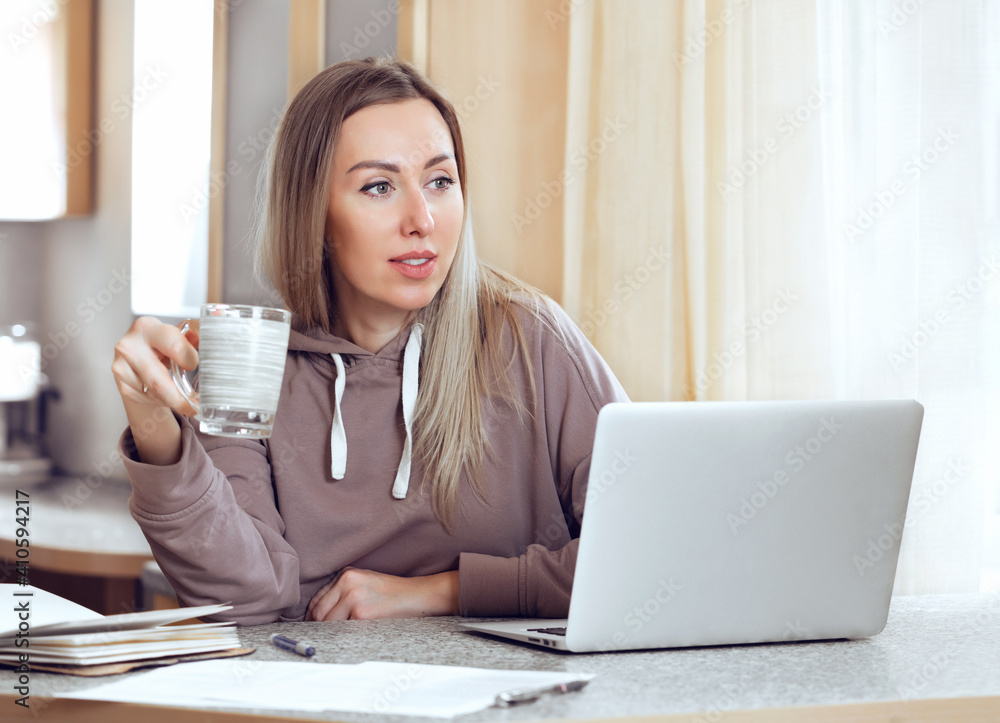 Remote learning or work. Young woman is browsing laptop with cup tea. Worker having break. Remote learning or work. Young woman is browsing laptop with cup tea. Worker having break.