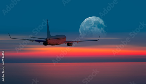 Passenger airplane flying away in to sky high altitude during sunset with full moon "Elements of this image furnished by NASA"