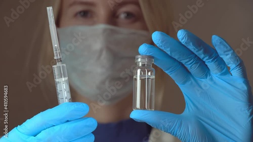 Portrait woman doctor in white hazmat protection holding vaccine ampoule in hand close-up. Coronavirus vaccination. New medication. Health care concept. photo