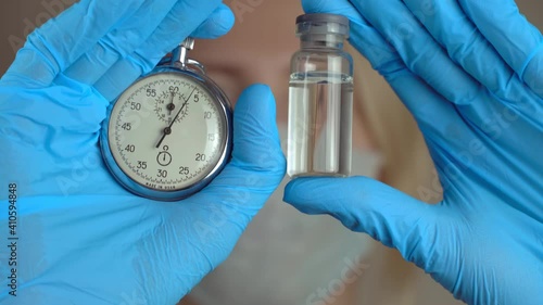 Portrait of female doctor in protective suit with an ampoule of vaccine in his hand and stopwatch close-up. new medicine. concept of development and timing of vaccination of world's population. photo
