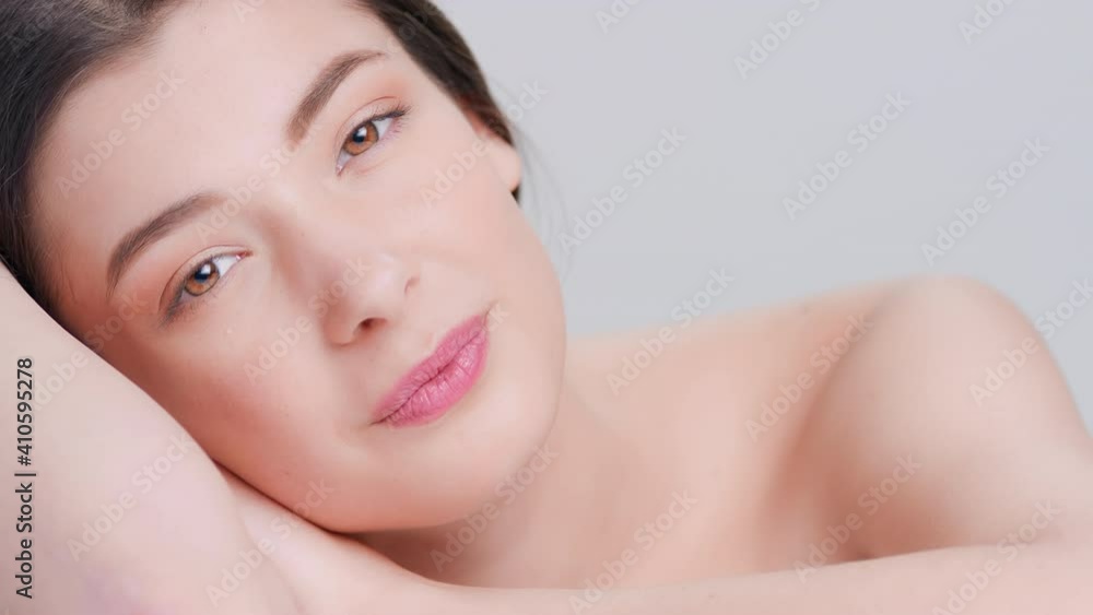 Close-up beauty portrait of young attractive woman lays her head on her hands and looks at camera on grey background | beauty products advertising concept