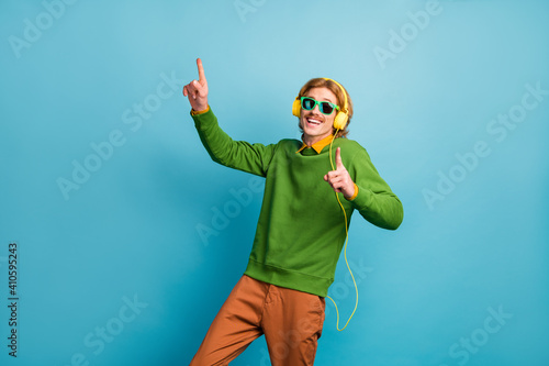 Photo of young happy positive funky funny man in sunglasses ang headphones dancing isolated on blue color background