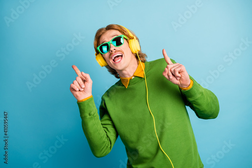 Photo of young happy positive good mood funky man in headphones sunglasses point finger copyspace isolated on blue color background photo