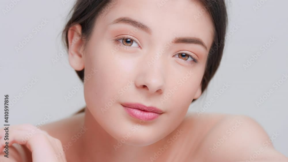 Extreme close-up beauty portrait of young dark-haired woman raises her head, touch her shoulder and looks at camera | Beauty face and skin care product commercial concept Extreme close-up beauty portrait of young dark-haired woman raises her head, touch her shoulder and looks at camera | Beauty face and skin care product commercial concept