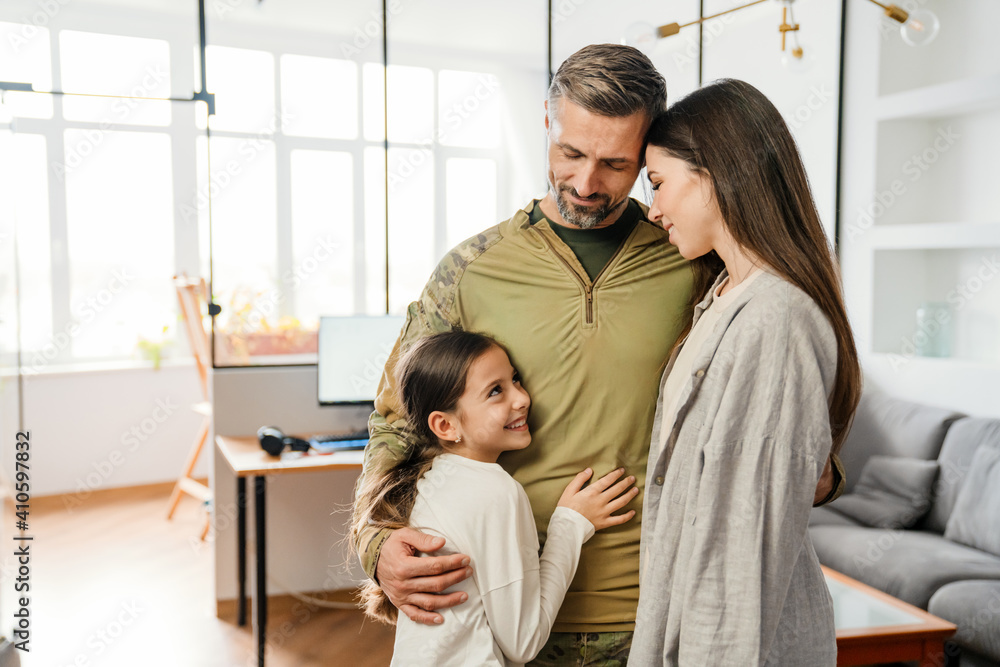 Happy masculine military man smiling and hugging his family indoors Happy masculine military man smiling and hugging his family indoors