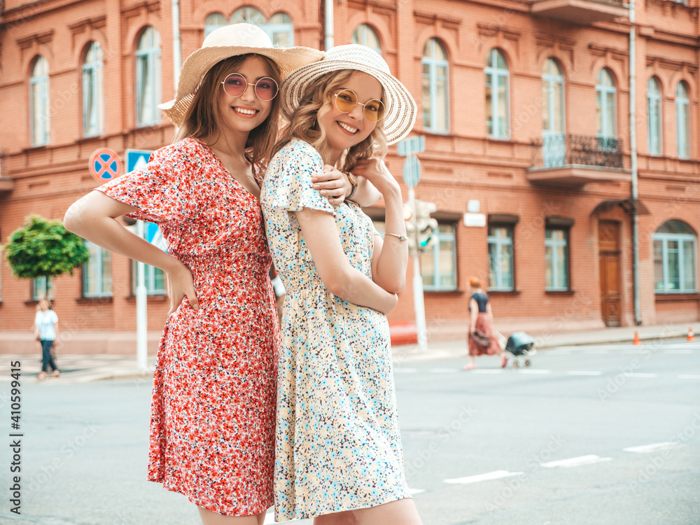 Two young beautiful smiling hipster female in trendy summer sundress.Sexy carefree women posing on the street background in hats. Positive models having fun and hugging