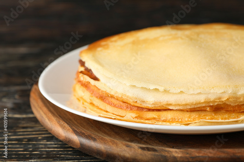 Board with thin pancakes on wooden background