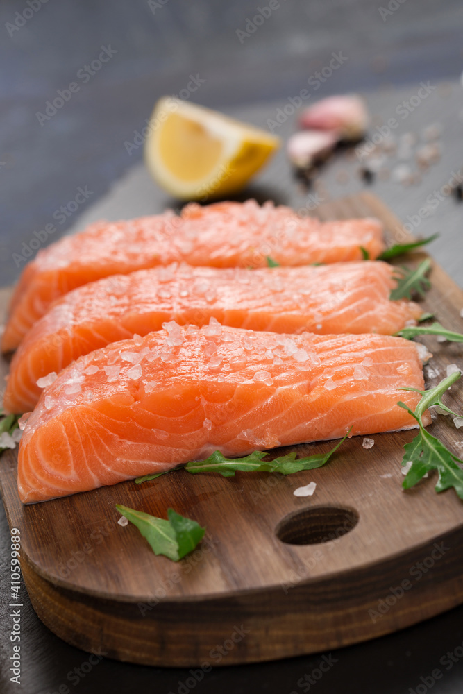 Raw fillet of salmon with sea salt, lemon and pepper on black stone background. Raw fillet of salmon with sea salt, lemon and pepper on black stone background.