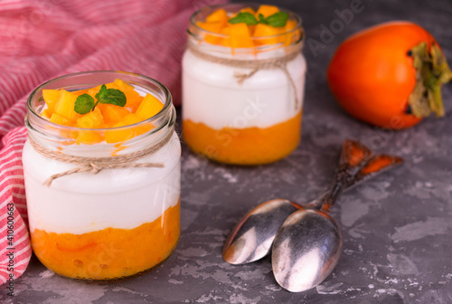 Two jars of yogurt with persimmon on a gray background.