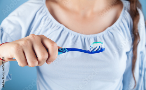 A girl holding a toothbrush on a blue background.