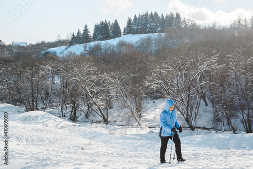 Senior woman climbing a hill using Nordic walking sticks. Active lifestyle, adventure concept. Nordic walking in winter.