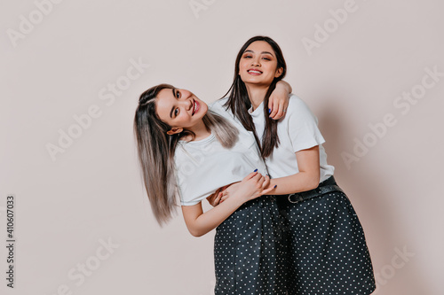 Fotografie Asian girls in identical skirts and blouses posing on beige background