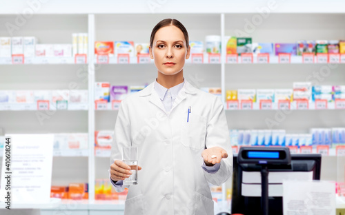 medicine, profession and healthcare concept - female doctor with pill and glass of water over pharmacy background