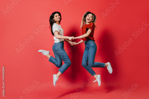 Happy Asian women in stylish T-shirts and jeans trousers jumping on isolated background