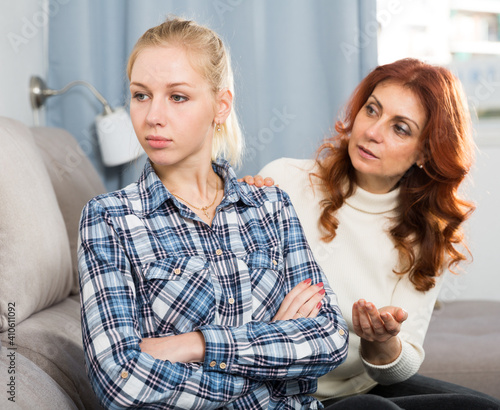 Tableau sur toile Unhappy girl sitting at sofa after conflict at home interior, mother talking wit