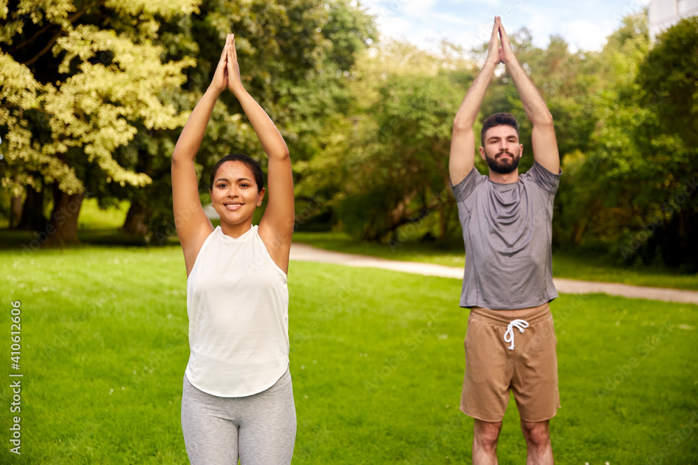 fitness, sport and healthy lifestyle concept - happy people doing yoga at summer park