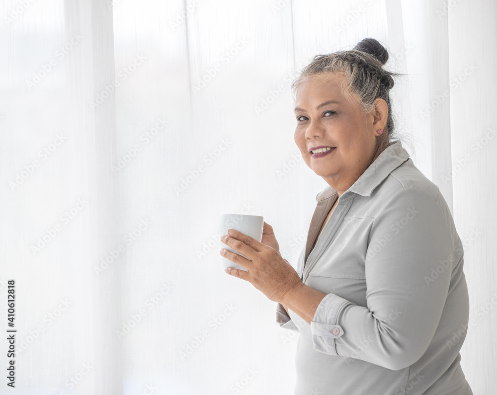An older senior grey hair Asian woman holding cup of coffee in hand with relax pose An older senior grey hair Asian woman holding cup of coffee in hand with relax pose