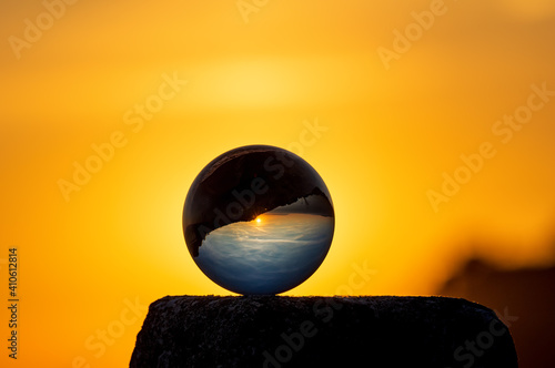 A glass ball standing on a stone reflects an sunset and a sky