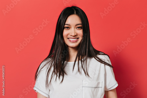 Lady with brown eyes is smiling on red background. Asian looking at camera