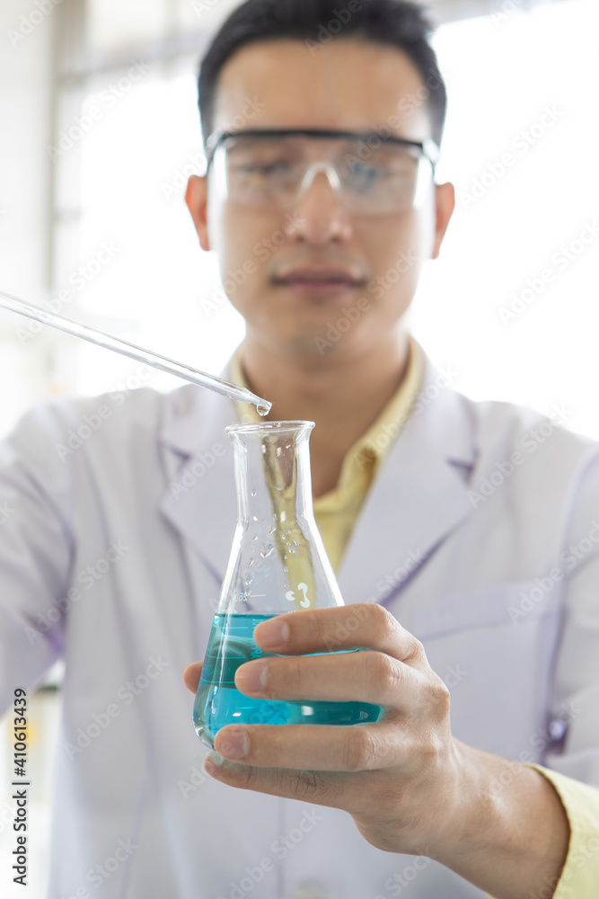 Young and good looking researcher wearing safety protective eyesglassed working in laboratory with blue liquid in test tube Young and good looking researcher wearing safety protective eyesglassed working in laboratory with blue liquid in test tube