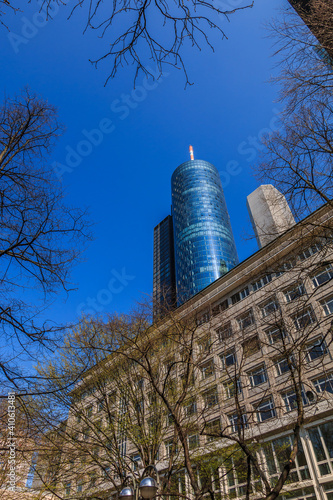 Skyscraper of the Frankfurt skyline. High-rise buildings with glass facade from the financial district in the center of the city. Trees at sunny day with blue sky in spring