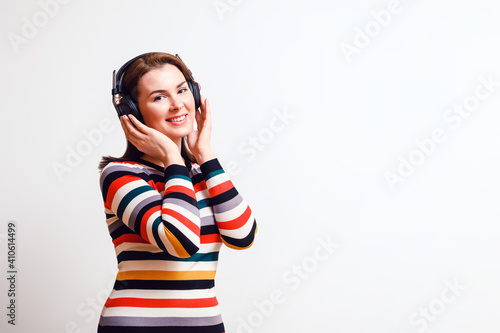 beautiful woman listens to music in isodynamic full-size closed wireless headphones, looks into the camera and smiles. Copy space to the right © Shauerman