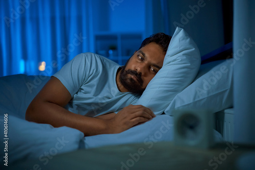 sleeping, insomnia and people concept - sleepless indian man lying in bed at home at night
