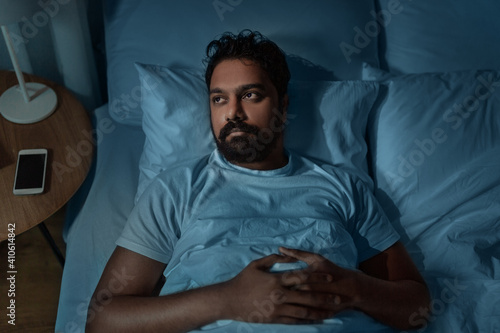 sleeping, insomnia and people concept - speelpess indian man lying in bed at home at night photo